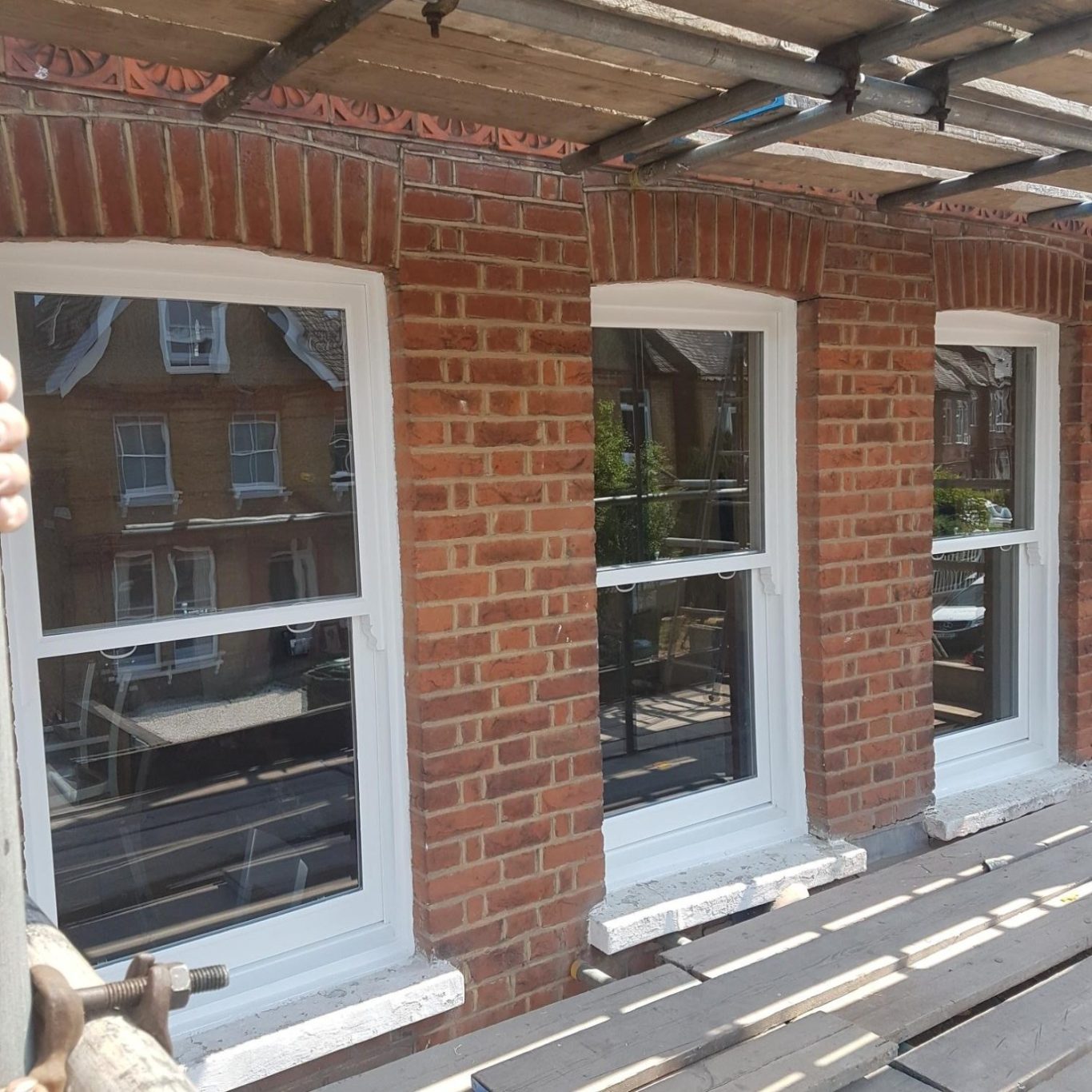 Georgian house with timber sash windows, London Three white-framed windows on a red brick wall, with scaffolding above.