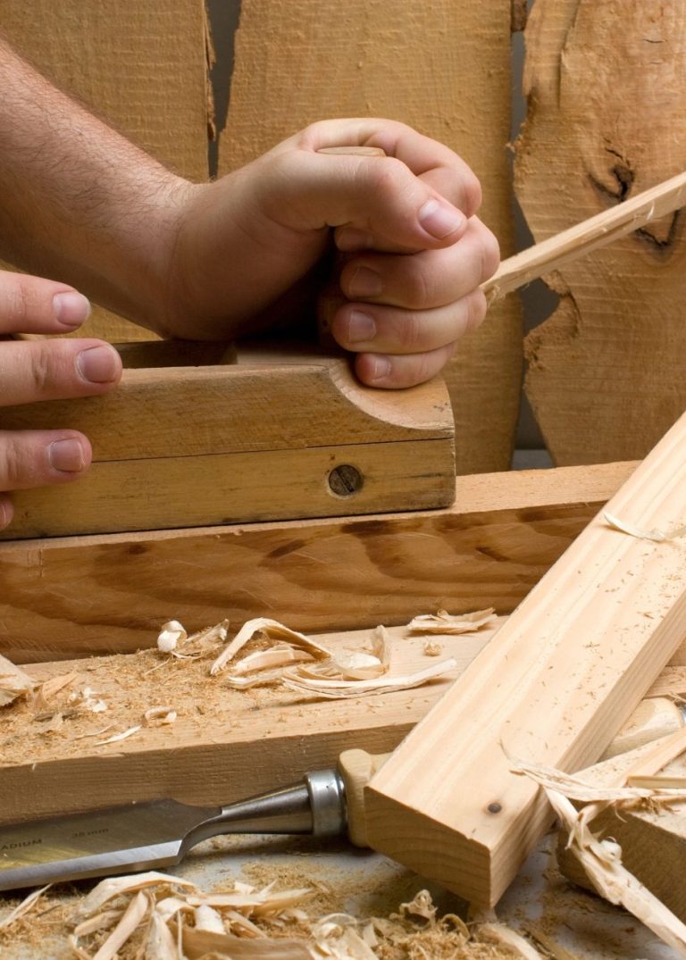 joinery work Hands using a hand plane on wood, surrounded by shavings.